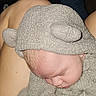 baby, sleeping, infant, child, portrait, close_up, gray_outfit, hooded_hat, lamb_hat, fluffy_clothing, cuddling, adult, arms, indoors, cozy, peaceful, soft_texture, blond_hair, zipper, photography