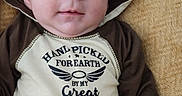 Noah is registered to the contest to win money with this photo: baby, infant, child, portrait, lying_down, blanket, hat, animal_hat, brown_clothing, onesie, face, eyes, wide_eyed, serious_expression, indoor, close_up, cozy, text_on_clothing, family_message, photography