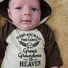 baby, infant, child, portrait, lying_down, blanket, hat, animal_hat, brown_clothing, onesie, face, eyes, wide_eyed, serious_expression, indoor, close_up, cozy, text_on_clothing, family_message, photography