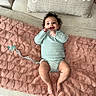 baby, infant, smiling, lying_down, blanket, heart_pattern, pacifier, onesie, couch, pillow, gratitude, indoor, happy, child, person, soft_texture, cozy, cute, home, relaxed
