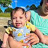 Elianys is registered to the contest to win money with this photo: baby, child, person, smiling, tongue_out, flower, earring, clothing, green_striped_top, sunlight, outdoor, blue_sky, clouds, trees, hand, holding, happy, cute, portrait, daytime