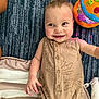 Beau is registered to the contest to win money with this photo: baby, child, smiling, onesie, beige, toy, carpet, striped_cushion, indoor, happy, cute, infant, reaching_out, playful, colorful_toy, blue_carpet, buttoned_onesie, lying_down, face, person