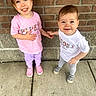 toddler, child, holding_hands, smiling, outdoor, sidewalk, brick_wall, concrete, pink_shirt, white_shirt, purple_pants, gray_pants, shoes, cute, happy, person, portrait, two_children, young_child, casual_clothing