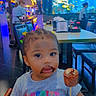 aquarium, chair, child, chocolate, clothing, colorful, cute, face, fish, food, hair_clips, indoor, mouth, people, restaurant, seated, smudge, stick_food, table, toddler