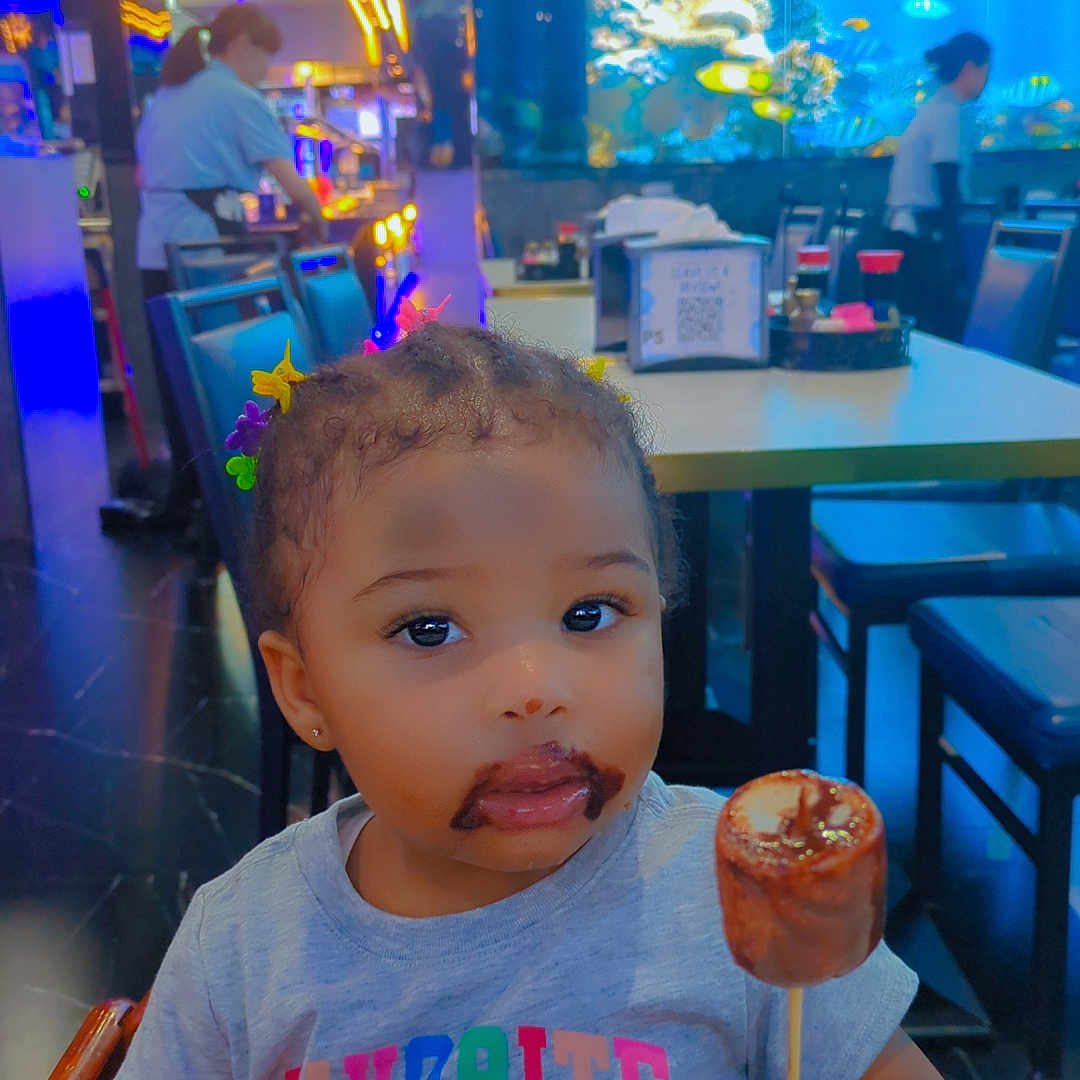Symiah F is registered to the contest to win money with this photo: aquarium, chair, child, chocolate, clothing, colorful, cute, face, fish, food, hair_clips, indoor, mouth, people, restaurant, seated, smudge, stick_food, table, toddler
