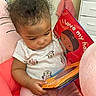 baby, child, reading, board_book, curly_hair, pink_clothing, minnie_mouse, plush_chair, indoor, nursery, cute, toddler, infant, person, seated, soft_toys, colorful, engaged, clothing, young_child