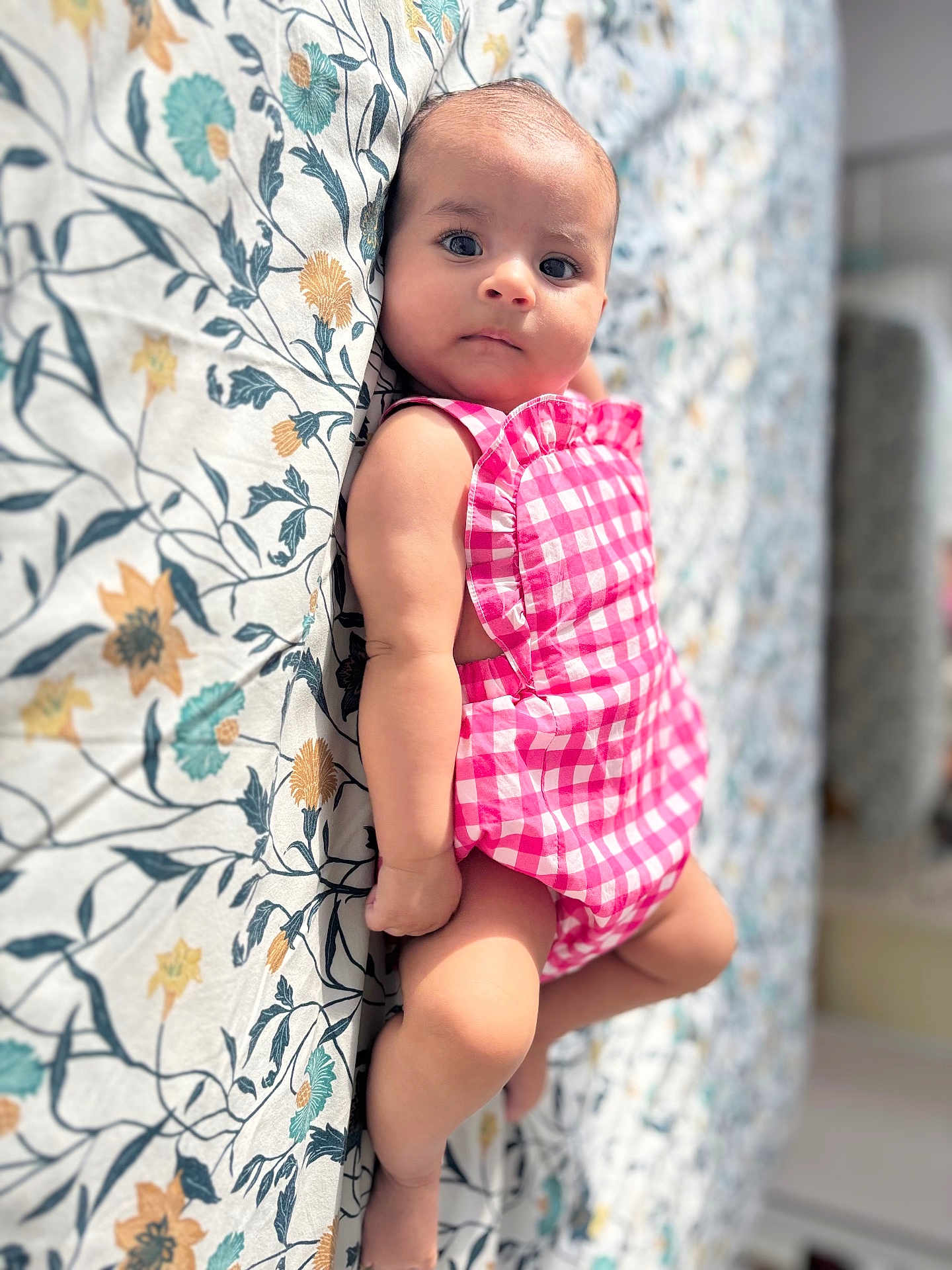 Ariella participe au concours pour gagner de l'argent avec cette photo : baby, infant, child, pink_gingham, romper, floral_bedspread, pattern, lying_down, curious, soft_light, indoor, cute, small, skin, face, eyes, arm, leg, bed, fabric