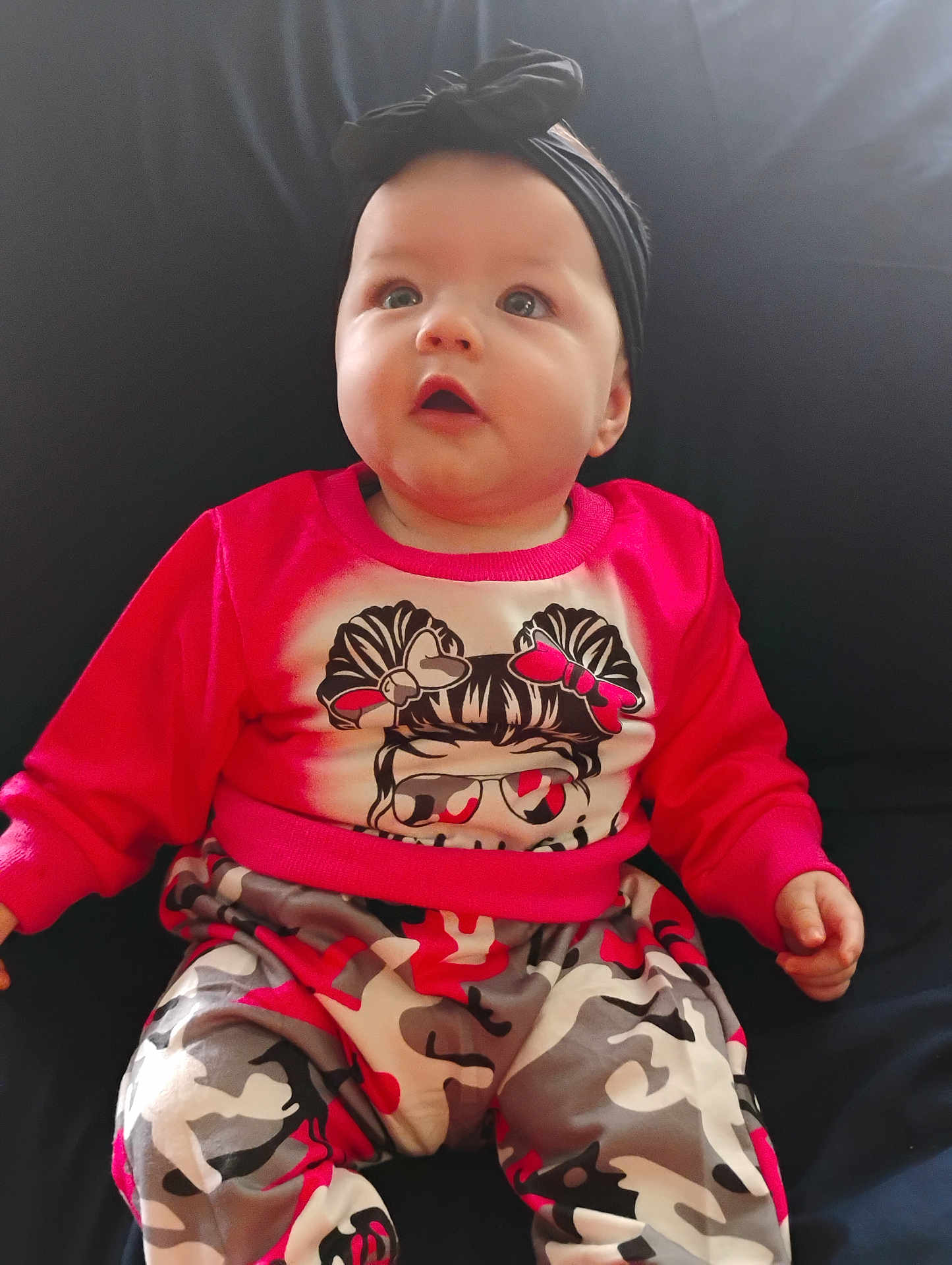 Ivy joined the competition — help win amazing prizes! baby, child, infant, red_clothing, headband, black_headband, bow, camo_pants, sitting, curious, indoor, portrait, cute, wide_eyes, looking_up, hands, face, young_child, casual_wear, colorful