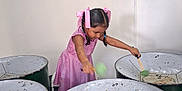 Ravisha is registered to the contest to win money with this photo: activity, braids, child, concentration, cultural, girl, green_drums, hands, indoor, music, musical_instruments, performance, person, pink_dress, pink_ribbons, playing, steel_drums, stick, white_wall, young