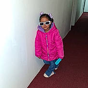 Ravisha is registered to the contest to win money with this photo: child, girl, sunglasses, pink_jacket, blue_jeans, sneakers, hallway, carpet, white_wall, standing, pose, cool, fashion, indoor, casual, young, person, accessory, toy, hair_bows