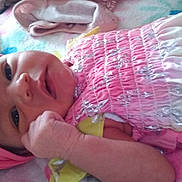 Billie is registered to the contest to win money with this photo: baby, infant, smiling, headband, pink, dress, butterfly_pattern, blanket, soft, cute, child, lying_down, hand, face, skin, indoors, cozy, colorful, closeup, newborn