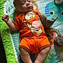 baby, infant, onesie, orange_clothing, plush_toy, play_mat, tigger, laying_down, child, cute, soft_light, indoor, colorful, expression, person, legs, arms, face, toy, floor_mat