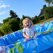 Emilio participe au concours pour gagner de l'argent avec cette photo : blonde_hair, blue_sky, casual_clothing, child, cute, daytime, fun, garden, greenery, happy, inflatable_pool, nature, outdoor, playing, portrait, smiling, summer, sunlight, toddler, vacation