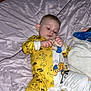 baby, child, bed, blanket, yellow_onesie, clothing, indoor, infant, person, cute, fabric, pattern, foot, hand, furniture, room, sleepwear, soft, portrait, curious