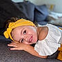 child, couch, cozy, curly_hair, cute, face, gray_furniture, hand, happy, headband, home, indoors, person, portrait, relaxed, resting, smiling, white_clothing, yellow, young