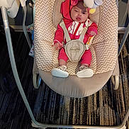 Gabriella is registered to the contest to win money with this photo: baby, infant, baby_swing, pink_clothing, toy, penguin_toy, indoor, carpet, footwear, straps, face, child, cushion, seat, playtime, expression, floor, pattern, hood, person