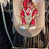 baby, infant, baby_swing, pink_clothing, toy, penguin_toy, indoor, carpet, footwear, straps, face, child, cushion, seat, playtime, expression, floor, pattern, hood, person