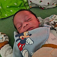 Noah a rejoint le concours — aidez-le/la à gagner de superbes lots ! baby, sleeping, mickey_mouse, bib, clothing, pillow, blanket, infant, soft_toys, cute, resting, indoors, cozy, child, face, person, comfort, nap, toddler, bed