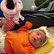 Annalise joined the competition — help win amazing prizes! baby, child, infant, stroller, orange_clothing, headband, bow, smiling, lying_down, portrait, face, toys, stuffed_animal, blanket, cushion, outdoor, vehicle, cozy, happy, photography