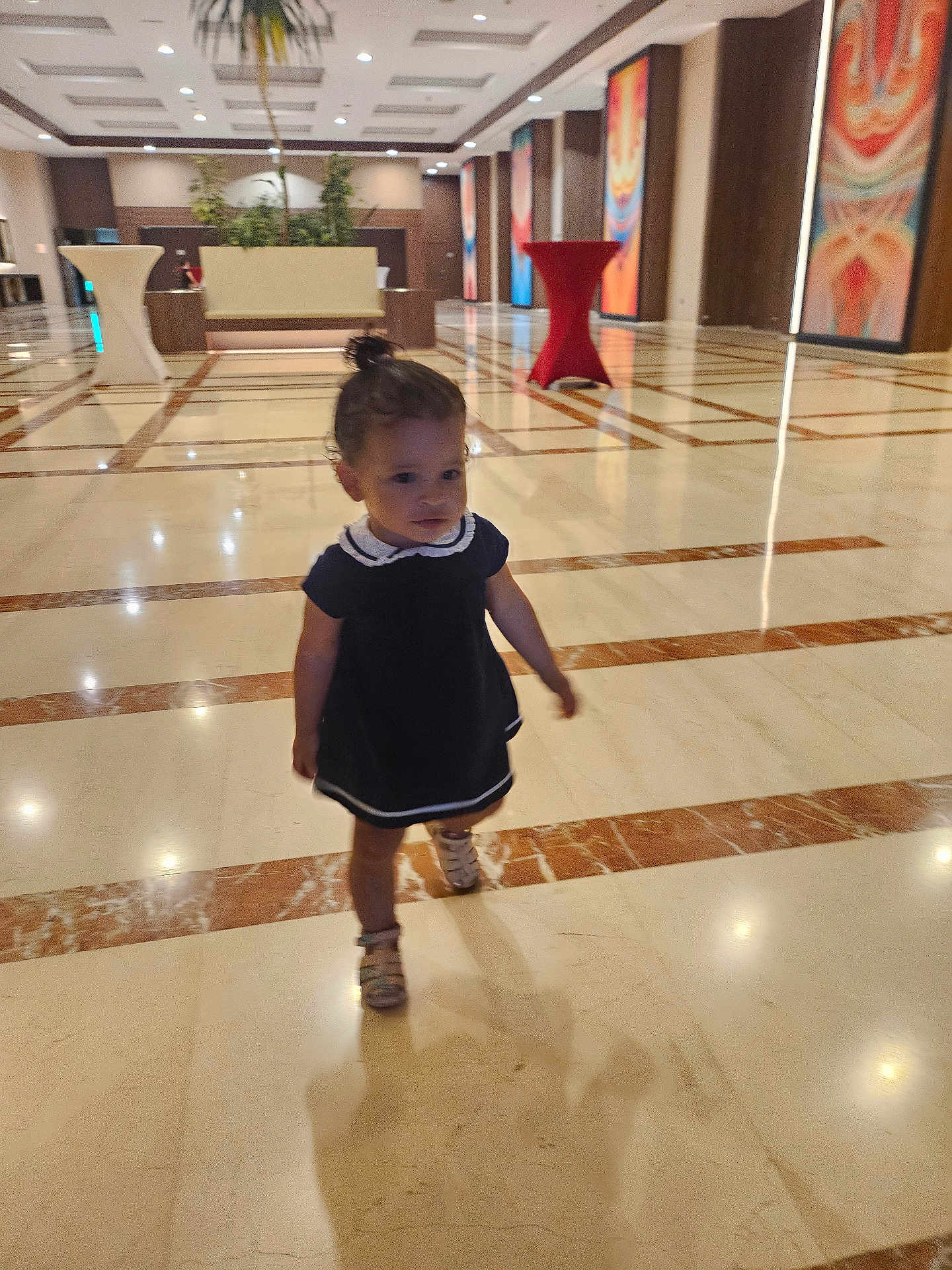 Inaya a rejoint le concours — aidez-le/la à gagner de superbes lots ! toddler, child, walking, marble_floor, lobby, indoor, dress, sandals, shadow, artwork, table, plant, ceiling_lights, person, hallway, wall_art, furniture, young_child, small_person, interior