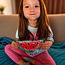 child, girl, smile, long_hair, sitting, cross_legged, blue_blanket, pink_pants, gray_socks, handmade_craft, watermelon, indoor, sofa, cute, happy, portrait, playful, colorful, art_project, cozy
