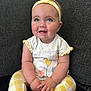 Mollie is registered to the contest to win money with this photo: baby, child, smiling, sitting, headband, yellow, white_shirt, flower_design, leggings, checkered_pattern, couch, indoor, happy, cute, infant, cheeks, hands, feet, portrait, young_child