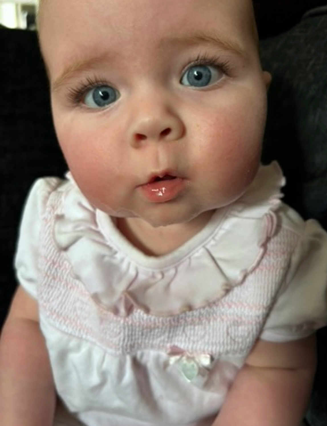 Mollie is registered to the contest to win money with this photo: baby, child, blue_eyes, face, closeup, curious, white_clothing, ruffled_collar, chubby_cheeks, infant, portrait, skin, cute, young_child, person, indoors, expression, head, mouth, sitting