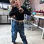 child, barefoot, jeans, black_top, heart_hands, playful, wooden_floor, christmas_tree, decorations, indoor, home, table, chair, mirror, toys, expression, blonde_hair, casual_clothing, holiday, festive