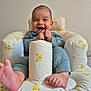 baby, smiling, infant, cushion, bear_pattern, blue_clothing, happy, feet, hands, seated, indoor, child, plush_seat, cute, joyful, comfort, playful, portrait, young, relaxed