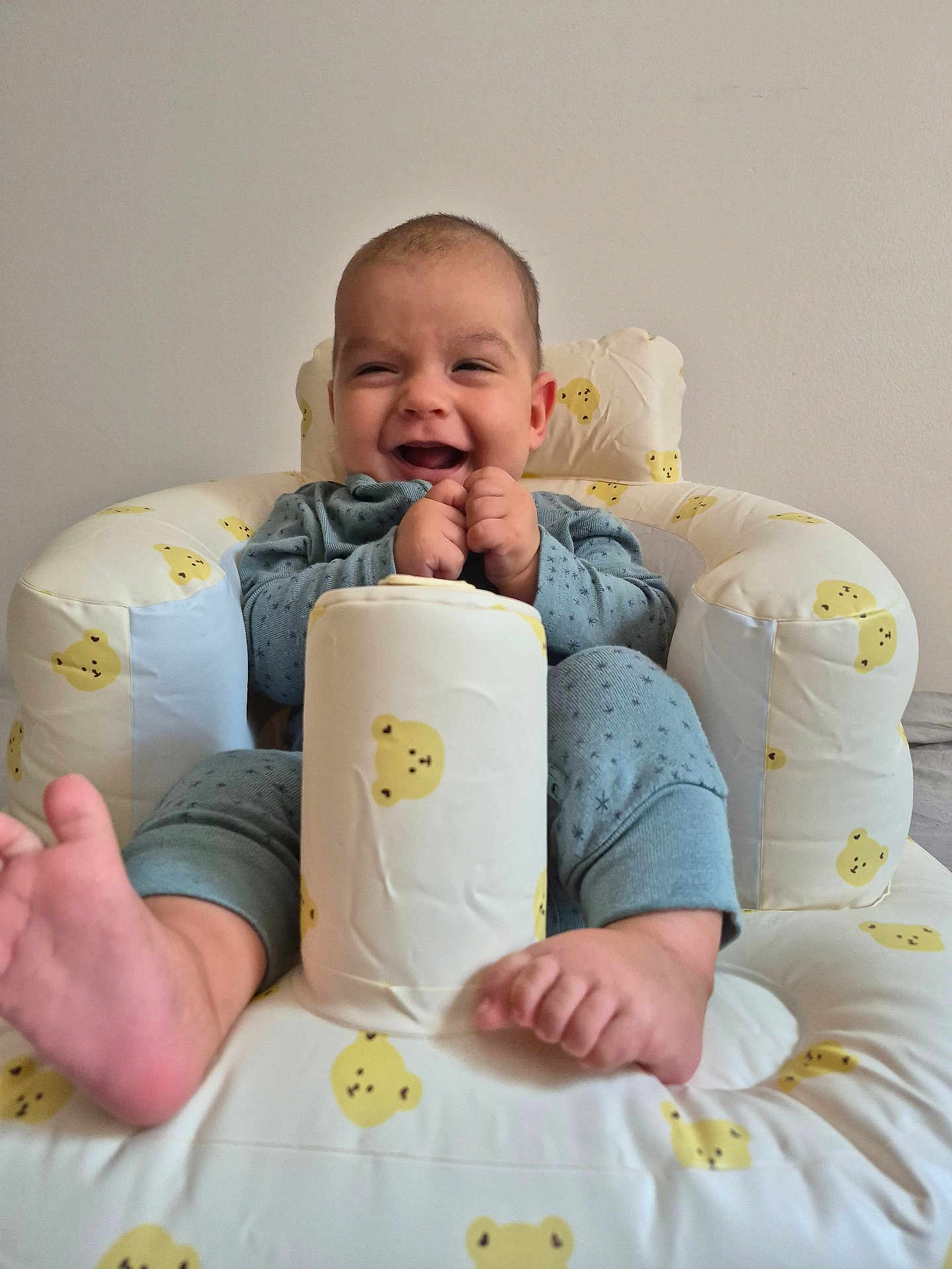 Calvin is registered to the contest to win money with this photo: baby, smiling, infant, cushion, bear_pattern, blue_clothing, happy, feet, hands, seated, indoor, child, plush_seat, cute, joyful, comfort, playful, portrait, young, relaxed
