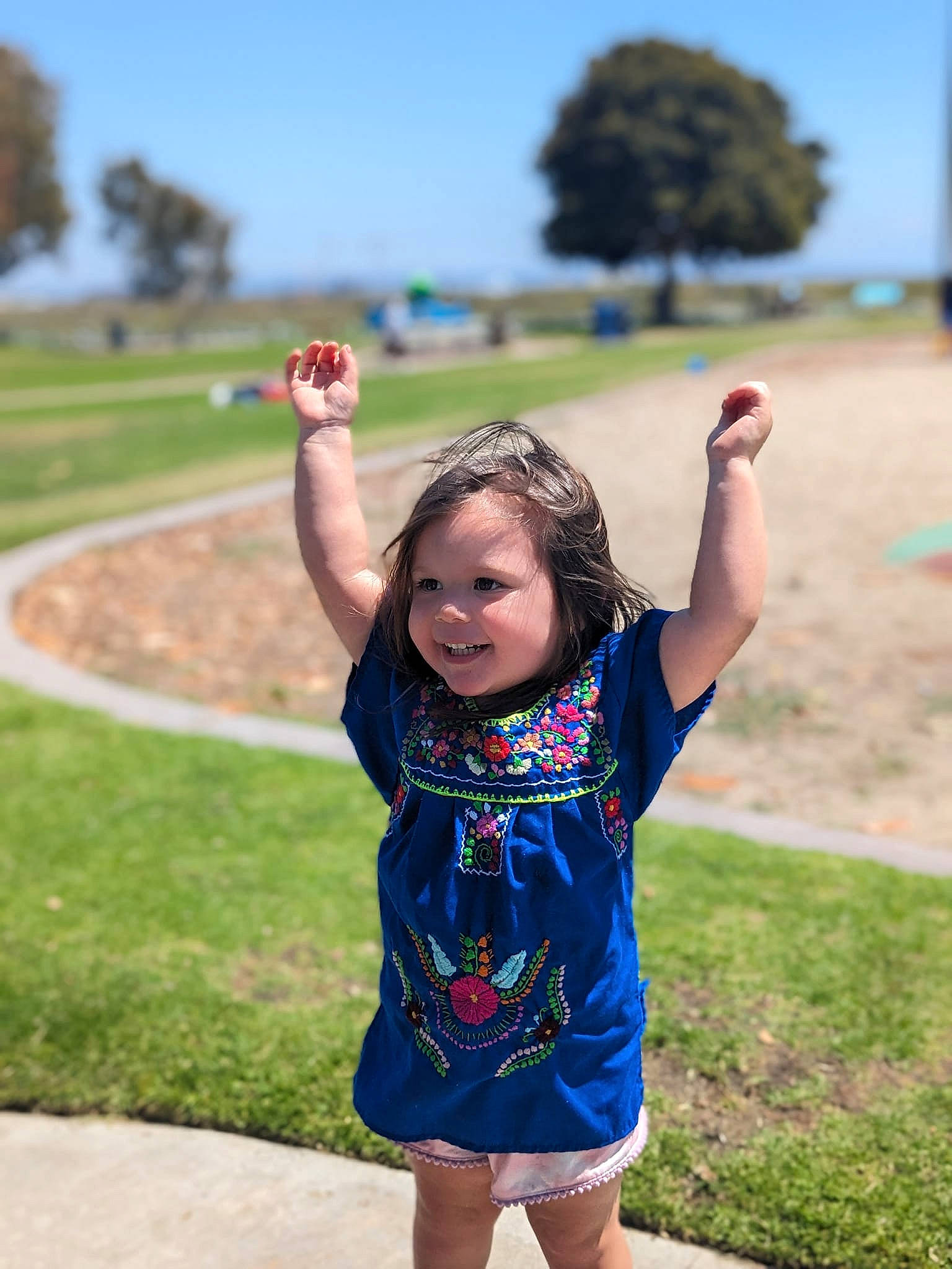 Estrella is registered to the contest to win money with this photo: daytime, electric_blue, fun, gesture, grass, grassland, happy, joy, leisure, people_in_nature, person, plant, recreation, road, shoulder, sky, sleeve, summer, t_shirt, toddler