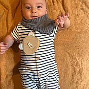 Evan participe au concours pour gagner de l'argent avec cette photo : baby, bear_shape, blanket, buttoned_clothing, child, cute, face, indoor, infant, lying_down, number_5, portrait, reaching_hand, scarf, skin, small_pockets, soft_lighting, striped_clothing, textured_fabric, wooden_toy