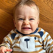 Lucien participe au concours pour gagner de l'argent avec cette photo : baby, child, face, smile, expression, striped_clothing, bear_design, wooden_floor, happy, cute, infant, portrait, playful, sitting, person, clothing, baby_clothes, indoors, skin, hand