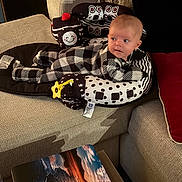 Lynette is registered to the contest to win money with this photo: baby, beige_furniture, checkered_pattern, child, comfort, couch, cushion, fabric, home, indoor, infant, landscape, onesie, person, photograph, plush, red_pillow, smiling_face, table, toy