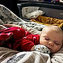 baby, sleeping, pajamas, red_clothing, blanket, cushion, bed, indoor, cozy, child, peaceful, infant, soft_texture, warm_lighting, face, hand, rest, cute, nursery, comfort