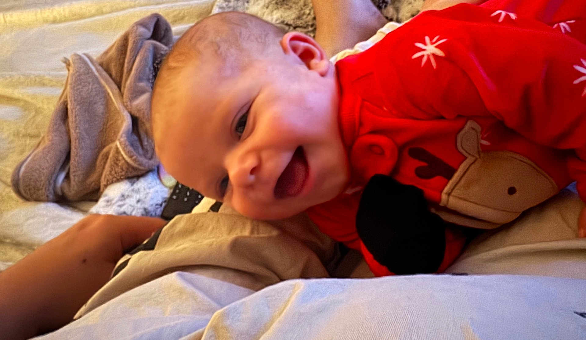 Lynette joined the competition — help win amazing prizes! baby, infant, smile, red_clothing, reindeer_design, blanket, bed, hand, happy, face, cheerful, cozy, indoors, child, cute, lying_down, warm_lighting, soft_texture, holiday_theme, person