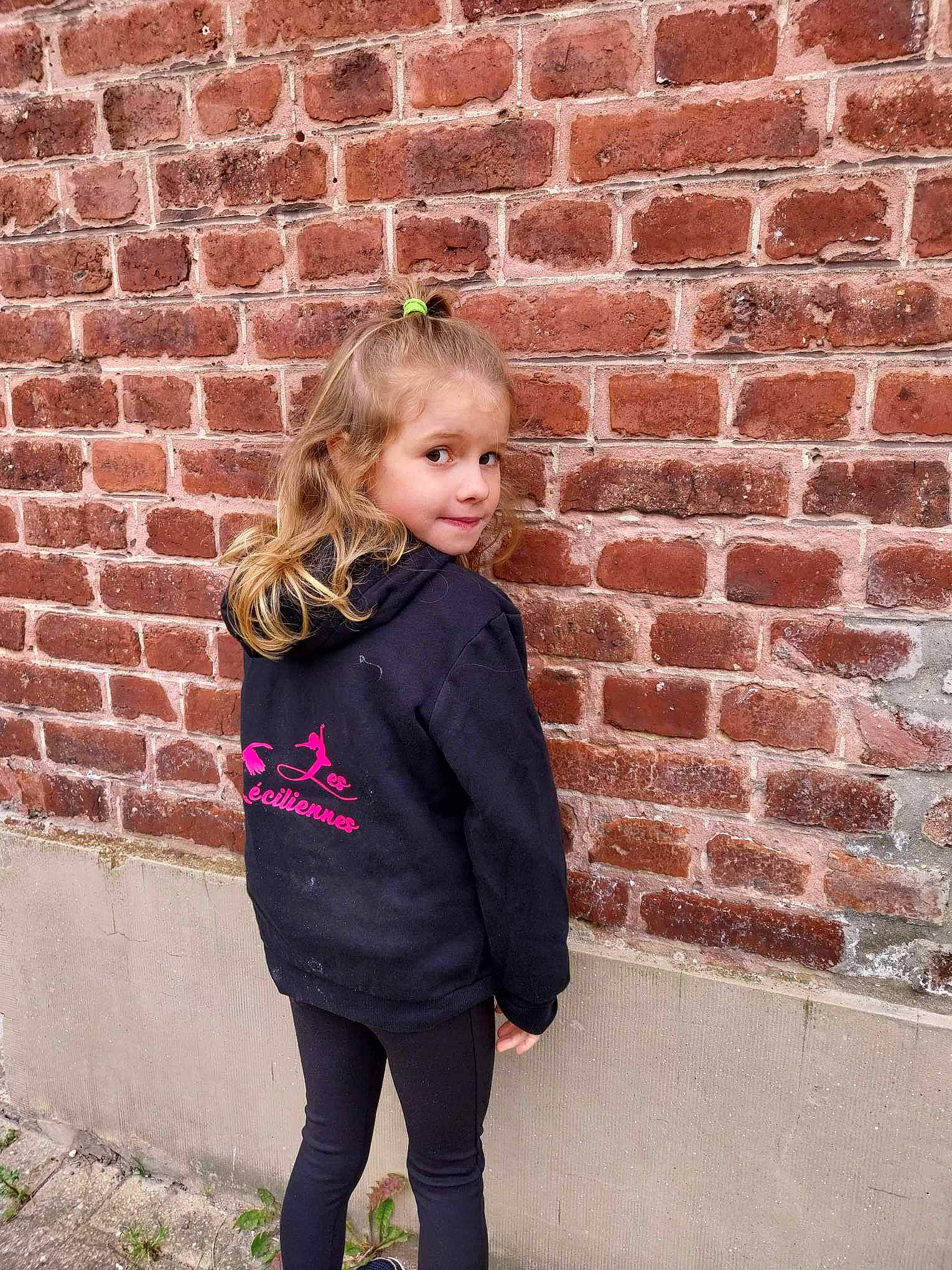 Augusta participe au concours pour gagner de l'argent avec cette photo : blond, brick, brickwork, brown_hair, chin, clothing, electric_blue, eye, hair, happy, head, lip, magenta, outerwear, pattern, person, pink, sleeve, standing, waist