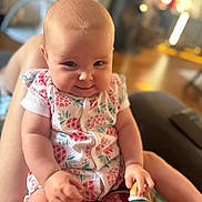 Gabrielle a rejoint le concours — aidez-le/la à gagner de superbes lots ! arms, baby, blurred_background, child, clothing, cute, face, hand, happy, indoor, infant, lap, legs, living_room, onesie, person, pineapple_pattern, smile, toy, warm_lighting