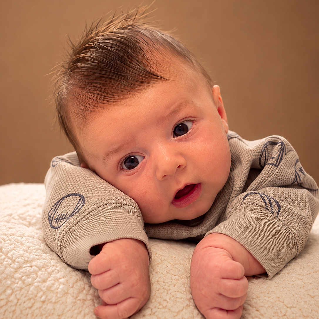 Gerald joined the competition — help win amazing prizes! baby, infant, child, portrait, closeup, lying_down, wide_eyed, surprised, smiling, face, hands, fingers, brown_hair, sweater, clothing, blanket, soft_texture, studio, warm_lighting, indoors