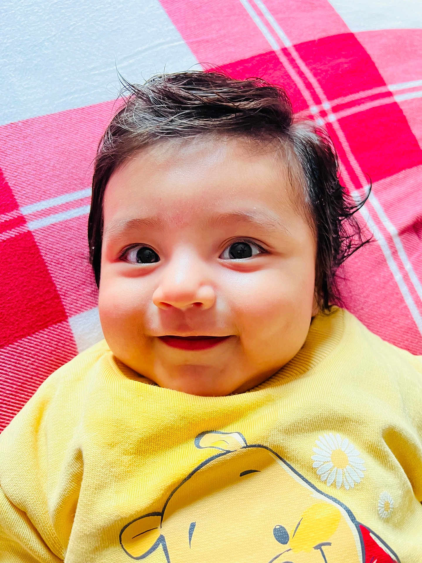 Liam is registered to the contest to win money with this photo: baby, child, smiling, face, portrait, yellow_shirt, cartoon, clothing, blanket, red, white, checkered, hair, cute, happy, indoors, infant, person, young, closeup