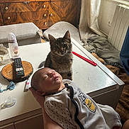 Aaron a rejoint le concours — aidez-le/la à gagner de superbes lots ! baby, infant, kitten, cat, table, remote_control, baby_bottle, pacifier, hand, blanket, furniture, window, curtain, wooden_cabinet, indoor, person, sleeping, cute, pet, cozy