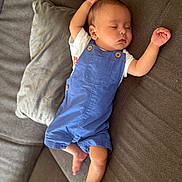 Joud a rejoint le concours — aidez-le/la à gagner de superbes lots ! baby, sleeping, blue_overalls, couch, pillow, arm_stretched, barefoot, infant, relaxed, indoors, child, face, peaceful, rest, comfort, toddler, clothing, furniture, home, portrait