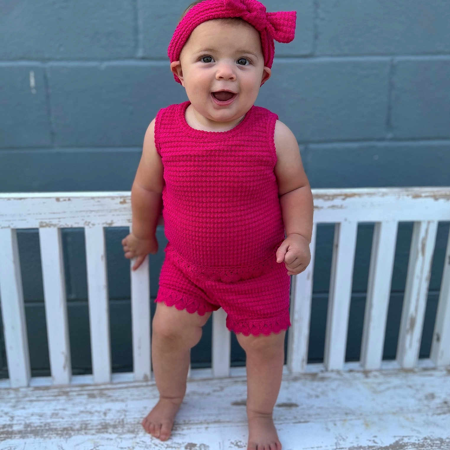 Sadie joined the competition — help win amazing prizes! baby, barefoot, bench, brick_wall, child, cute, fashion, happy, headband, infant, knitted_outfit, outdoor, person, pink_clothing, playful, portrait, smiling, standing, summer, wall