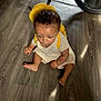 toddler, child, baby, floor, wooden_floor, backpack, yellow_backpack, curly_hair, sitting, indoors, barefoot, short_sleeve, light_beige_clothing, person, young_child, head, expression, casual, home, cute