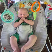 Ryder is registered to the contest to win money with this photo: baby, infant, child, activity_center, baby_seat, portrait, sitting, indoor, toys, rattle, jungle_theme, colorful, green_clothing, smiling, hands, fingers, bare_feet, furniture, playtime, home