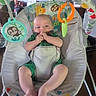 baby, infant, child, activity_center, baby_seat, portrait, sitting, indoor, toys, rattle, jungle_theme, colorful, green_clothing, smiling, hands, fingers, bare_feet, furniture, playtime, home