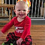 baby, child, smiling, plaid_pants, red_shirt, socks, wood_floor, fireplace, safety_gate, indoors, happy, person, candid, cheerful, pajamas, home, warm, cute, toddler, infant