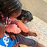 King Leonardo is registered to the contest to win money with this photo: child, children, dog, black_dog, carpet, rug, indoor, barefoot, pink_pants, blue_shirt, curly_hair, braids, beads, floor, cozy, pet, playing, home, casual_clothing, resting