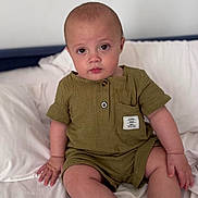 Shay is registered to the contest to win money with this photo: baby, bed, child, cute, expression, eyes, face, green_clothing, hands, head, indoor, infant, legs, pillow, portrait, romper, sitting, skin, soft_fabric, white_bed