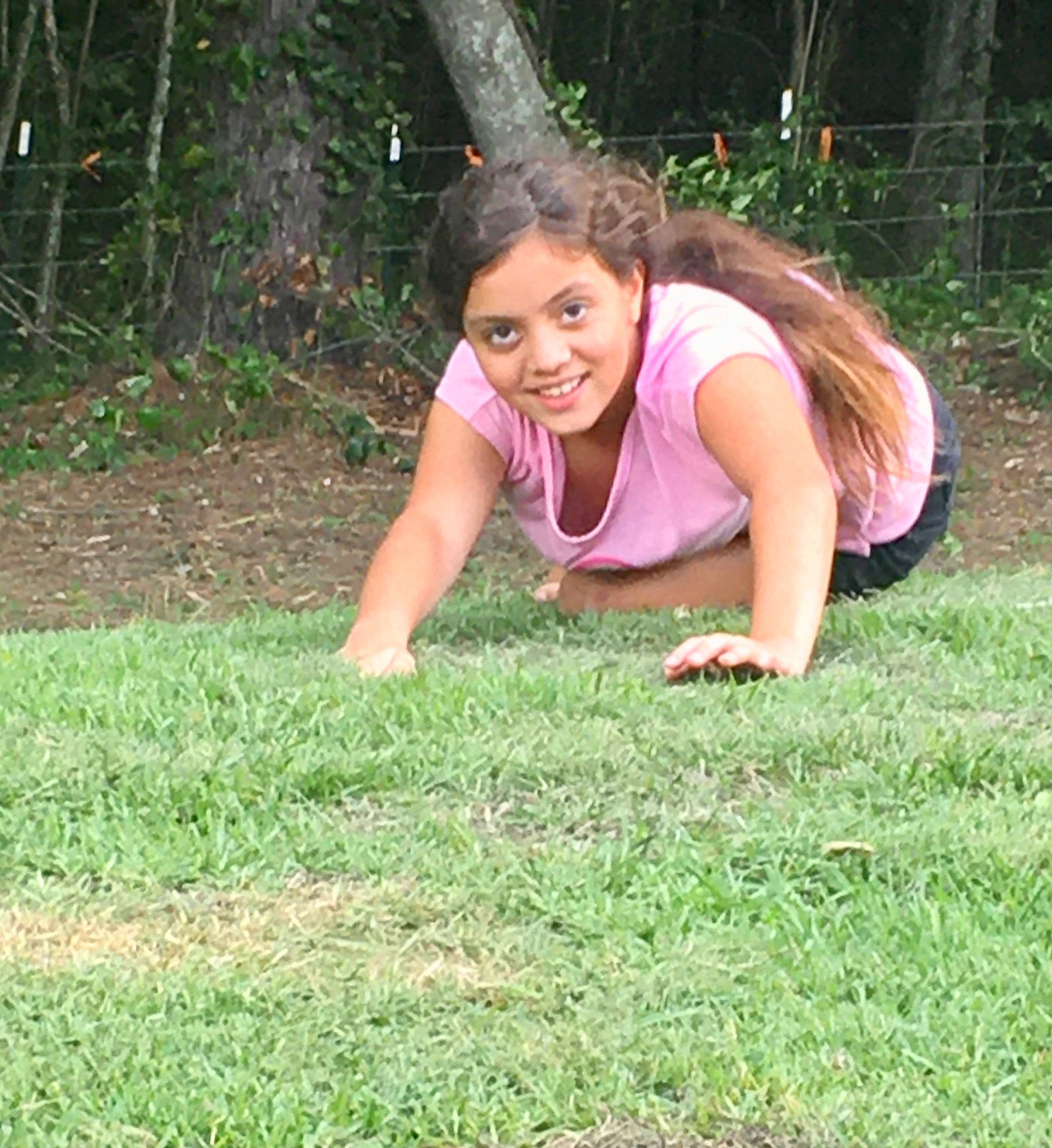 Klara is registered to the contest to win money with this photo: brown_hair, chest, child, eyewear, grass, grassland, happy, human_leg, joy, knee, lawn, leisure, long_hair, people_in_nature, person, plant, recreation, sitting, smile, t_shirt